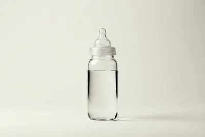 Un biberon en verre rempli d'eau minérale pure sur un fond épuré.