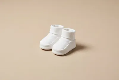 Petits chaussons de bébé blancs sur fond minimaliste beige.