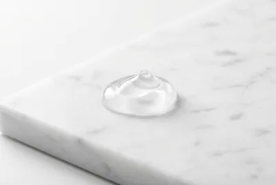 Goutte de gel lubrifiant pur sur fond de marbre blanc minimaliste.