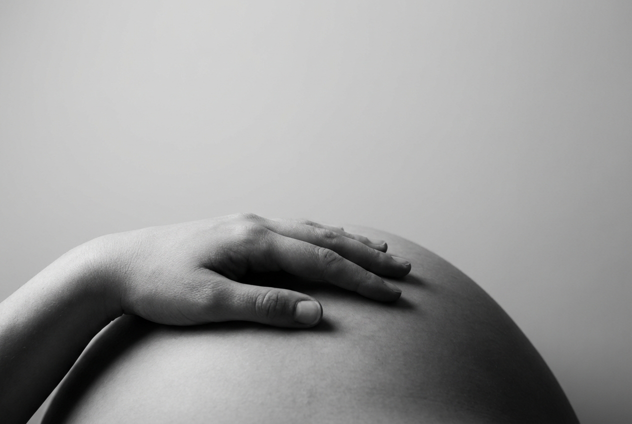 Peut-on sentir le cœur du bébé avec sa main sur le ventre ? Composition minimaliste d'une main sur un ventre rond de femme enceinte, fond neutre et épuré.