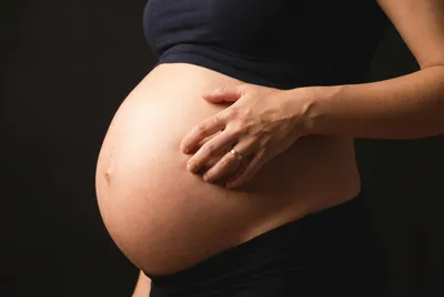 Miniature d'une main grattant délicatement un ventre de femme enceinte, composition minimaliste.