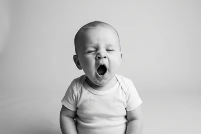 Portrait minimaliste d'un bébé qui bâille, symbole de la fatigue infantile.