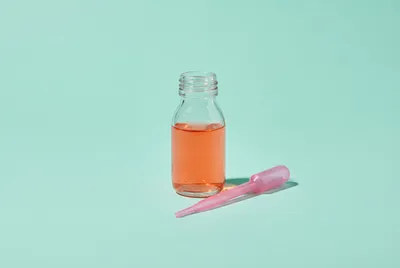 Bouteille de sirop pour enfant et sa pipette doseuse rose sur un fond épuré.